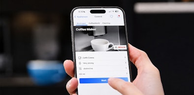 Hand bedient een Bosch koffiemachine op afstand via de Home Connect app op een telefoon