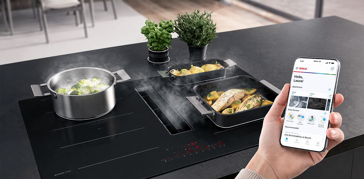 Smartphone met Home Connect app naast een Bosch kookplaat met afzuiging
