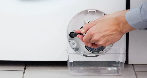 Hand draait pompfilter los bij serviceklep van Bosch wasmachine met opvangbak eronder