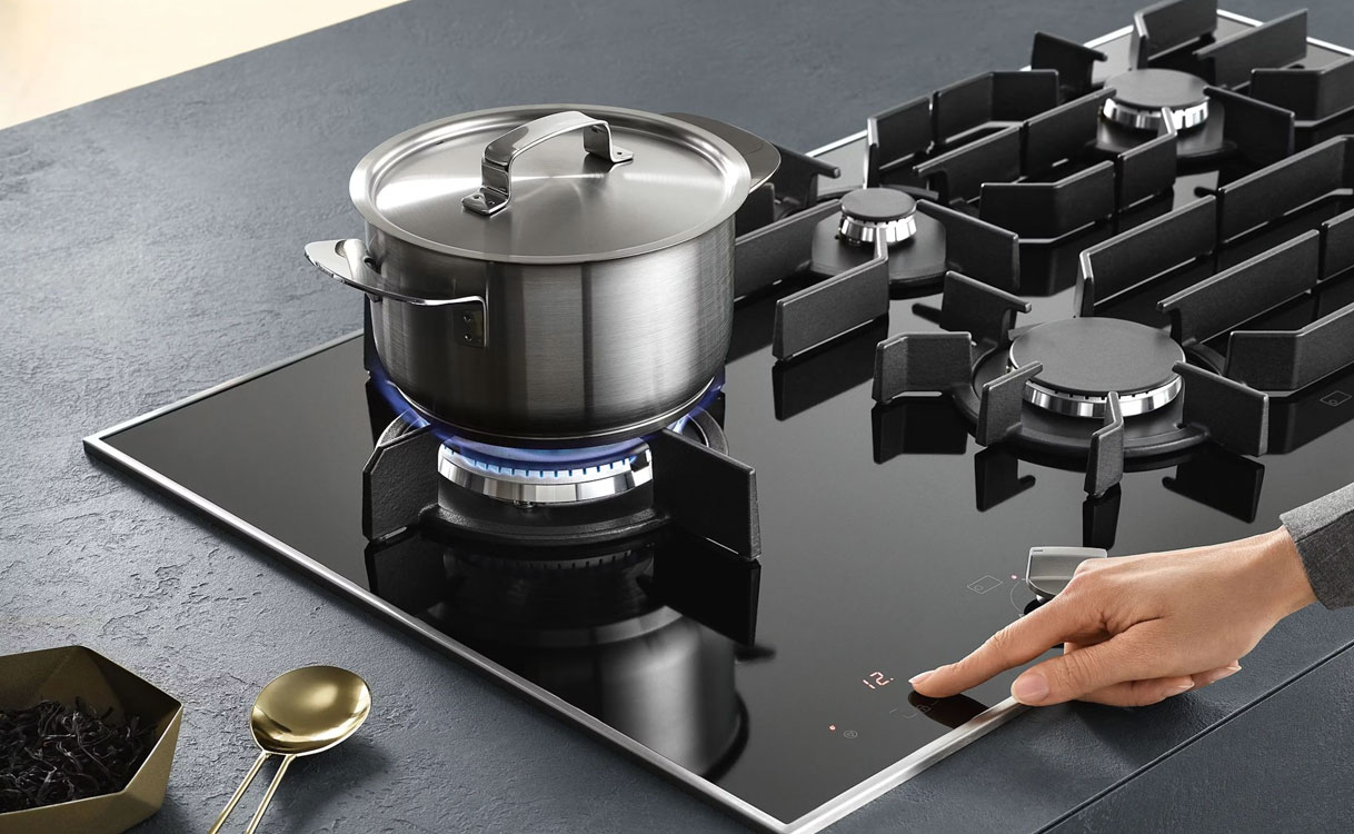 Gas op glas kookplaat met vijf gasbranders, gietijzeren pannendragers en een pan op de grote brander