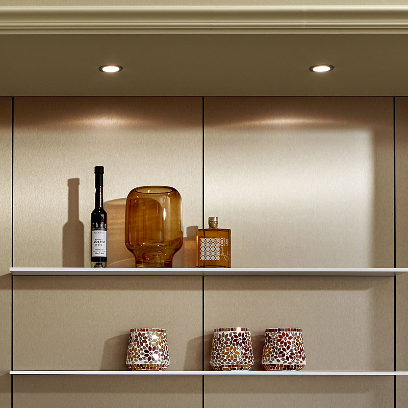 Bronskleurige achterwand met planken en ingebouwde spots.