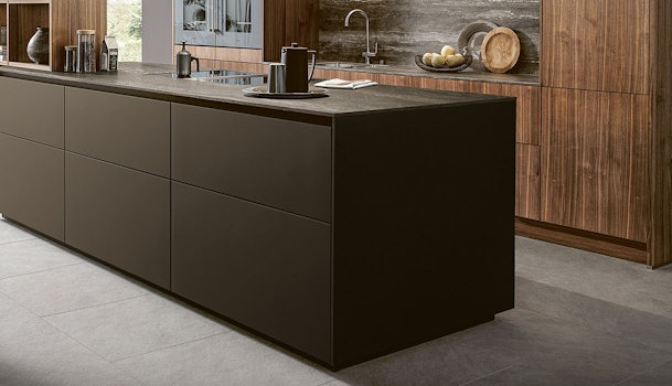 Moderne chocoladebruine keuken met groot kookeiland, donker werkblad en wandkasten in houtfineer.