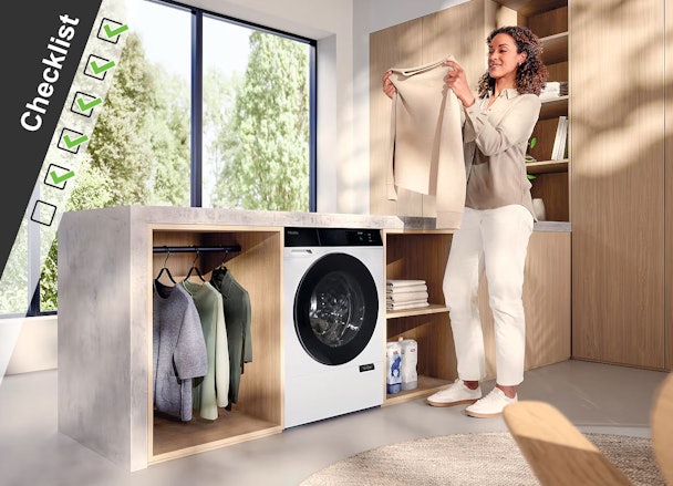 Vrouw bij ingebouwde wasmachine die schone kleding controleert in moderne wasruimte