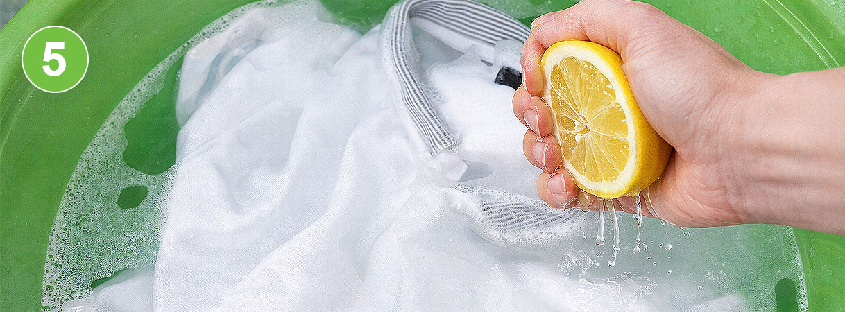 Citroensap uitknijpen boven witte was: hand knijpt halve citroen uit boven wit textiel in een teiltje met sopwater