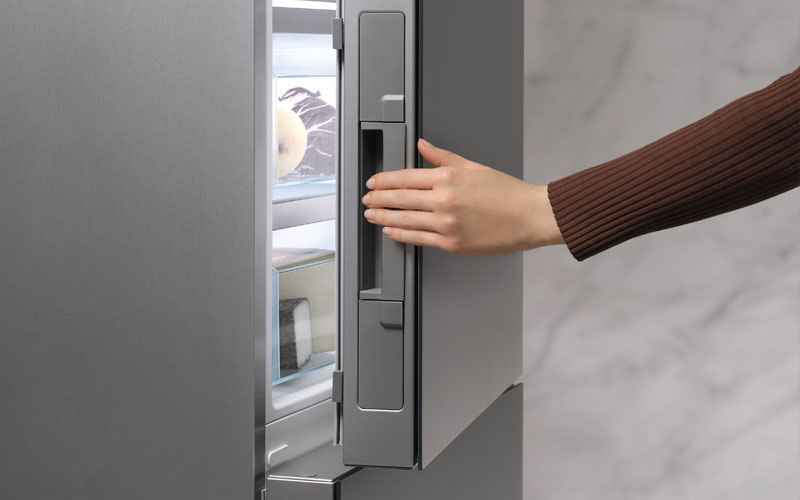 Hand opent Miele vriezerdeur met Click2open systeem voor moeiteloze bediening