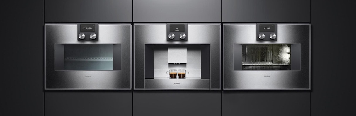 Het lijnenspel van een naast elkaar ingebouwde compacte combi-oven, koffiemachine en stoomoven.