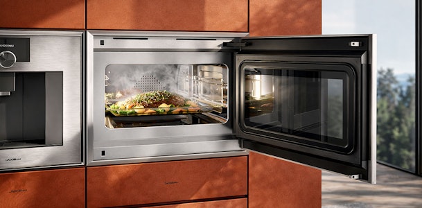 Gaggenau combimagnetron met open deur en dampende maaltijd in luxe koper keuken voor veelzijdig koken