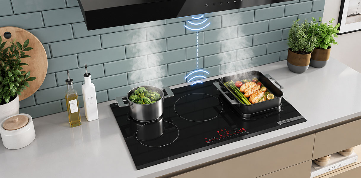 Inductie kookplaat met een pan broccoli en een braadslede, met een draadloos signaal naar de afzuigkap erboven