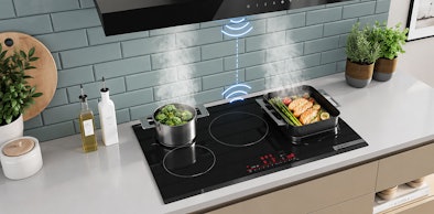 Inductie kookplaat met een pan broccoli en een braadslede, met een draadloos signaal naar de afzuigkap erboven