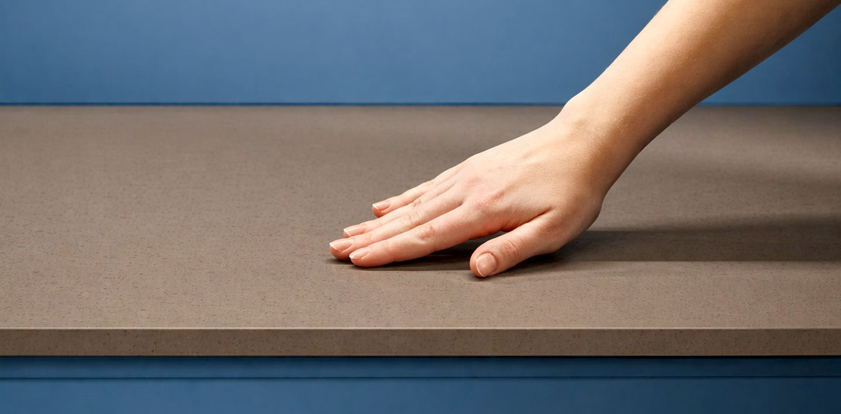 Hand voelt over composiet werkblad in beige tint op blauwe ondergrond