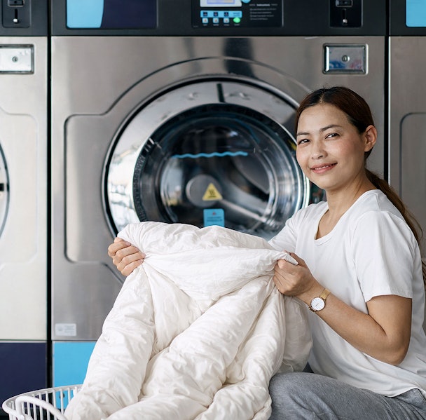 Vrouw met dekbed bij industriële wasmachine in wasserette