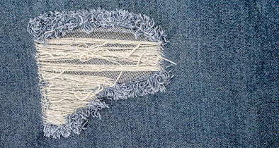 Destroyed jeans met scheuren en losse draden die verder beschadigen in droger