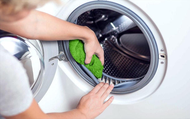 Hand die het rubberen deurrubber van een wasmachine schoonmaakt met een doek