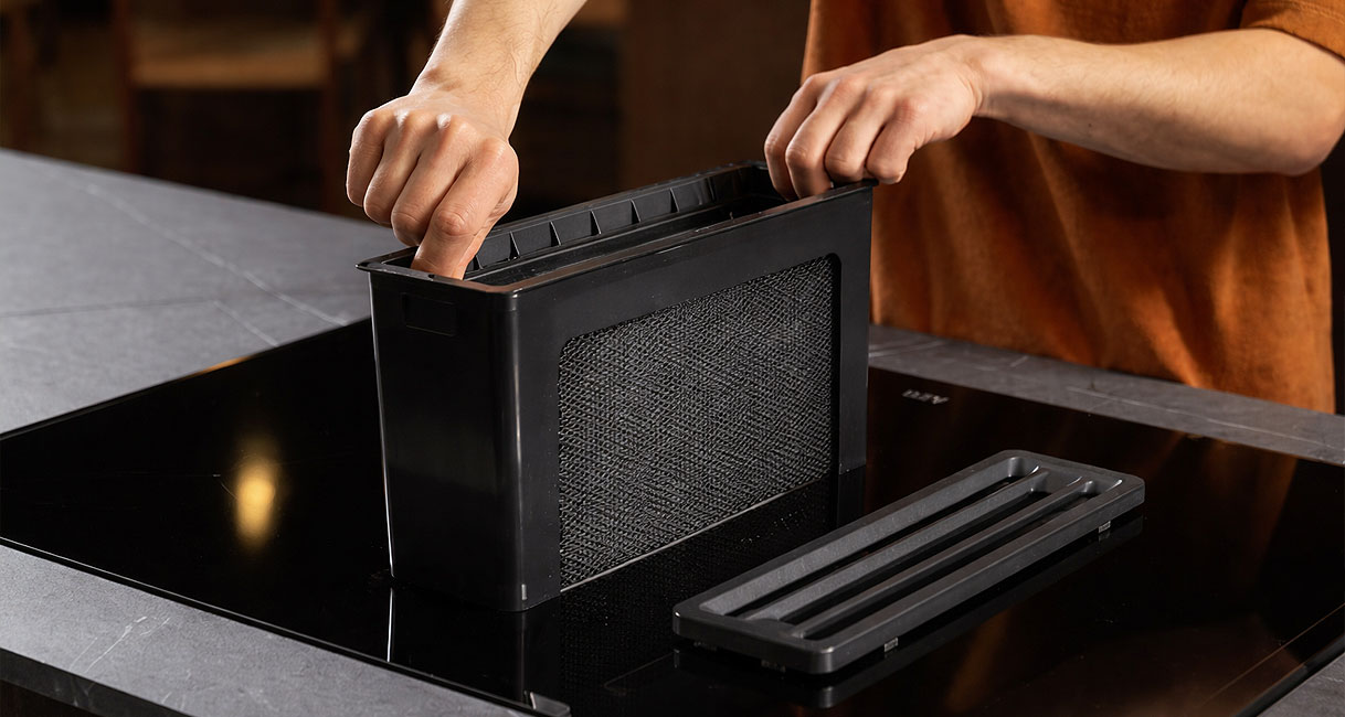 Persoon verwijdert vetfilter van kookplaat met geïntegreerde afzuiging voor eenvoudige reiniging in de vaatwasser