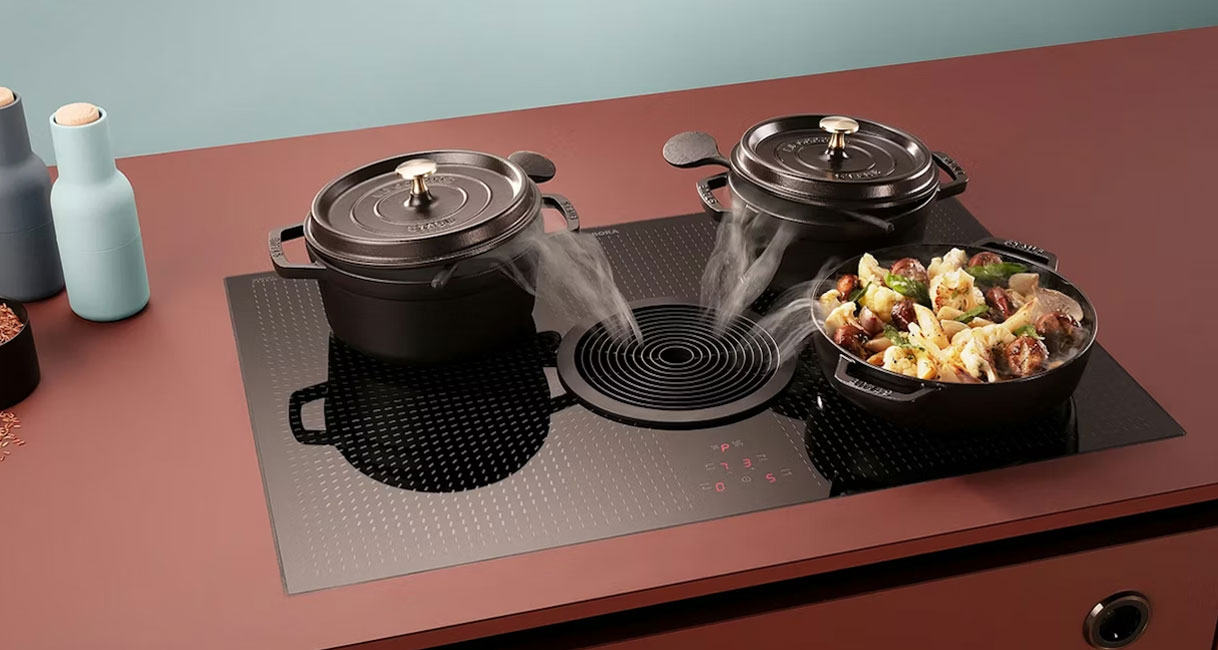 Kookplaat met geïntegreerde afzuiging die kookdampen direct bij de bron naar beneden zuigt terwijl pannen op het vuur staan