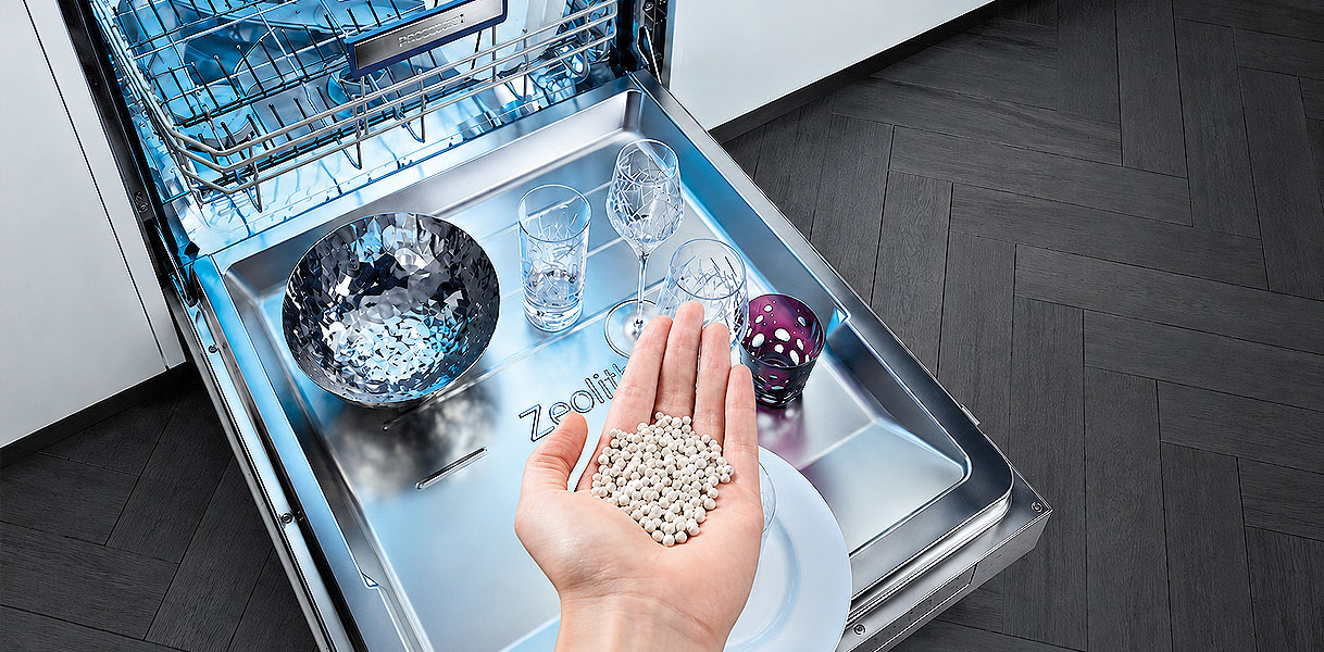 Hand met zeoliet korrels bij een vaatwasser die de vaat zonder extra stroom droogt