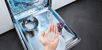 Hand met zeoliet korrels bij een vaatwasser die de vaat zonder extra stroom droogt