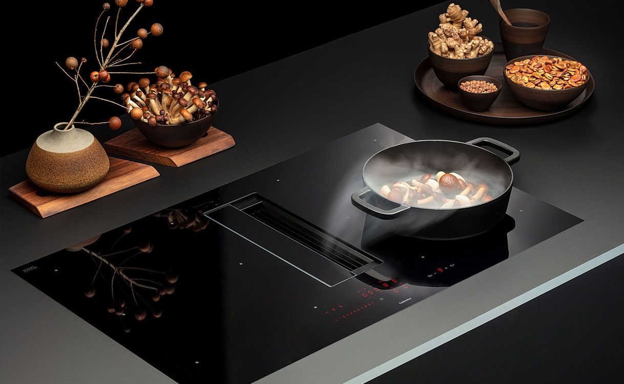 Falmec kookplaat met geïntegreerde afzuiging en pan met stoom op zwart glazen kookoppervlak.