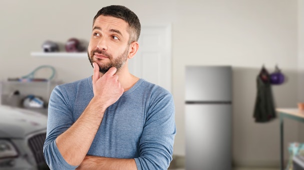 Man die nadenkt in een schuur met koelkast op de achtergrond, illustratie bij veelgestelde vragen over 0 °C-ready koelkasten