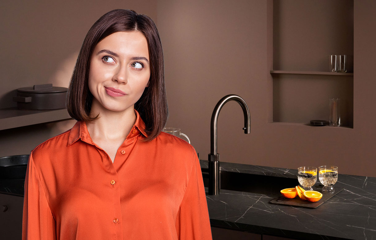 Vrouw kijkt vragend opzij in moderne keuken met Quooker Fusion Round in Gunmetal op donker marmeren aanrecht