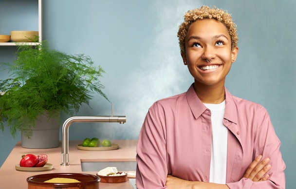 Vrouw kijkt vragend omhoog in moderne keuken met Quooker Fusion kraan in RVS waaruit stoom komt