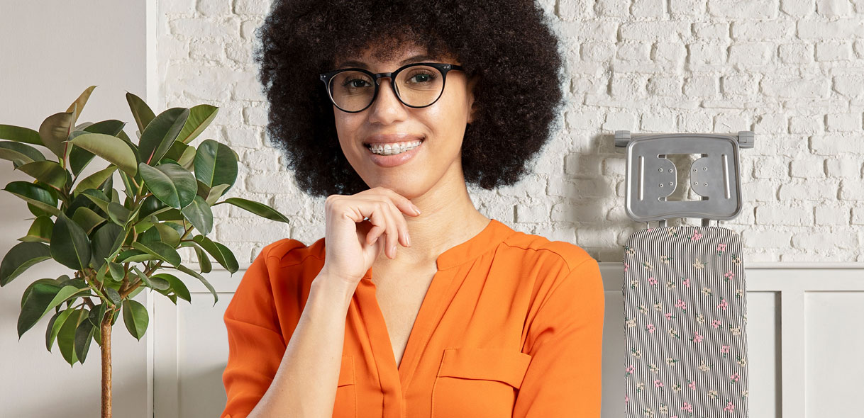 Vrouw met bril glimlacht in wasruimte met strijkplank op achtergrond