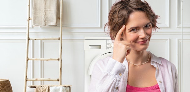 Vrouw met nadenkende blik voor een wasmachine in een lichte wasruimte
