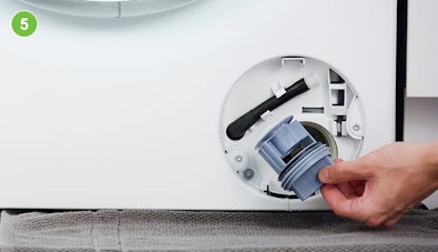 Hand trekt het grijsblauwe pompfilter volledig uit het filtercompartiment van een wasmachine