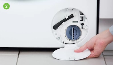 Hand houdt het geopende filterklepje van een wasmachine vast, het pompfilter en de zwarte noodafvoerslang zijn zichtbaar