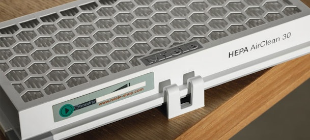 Close-up van Miele HEPA AirClean 30 filtercassette met honingraat en timestrip op een tafel, voorbeeld van HEPA-stofzuigerfilter voor prijsvergelijking en energiebesparing.