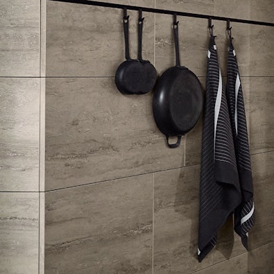 Zwart ophangsysteem met pannen aan lichte travertinwand