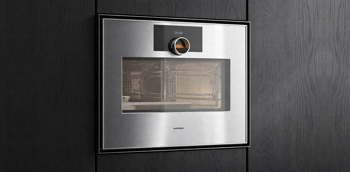 Gaggenau Expressive serie combimagnetron in RVS met draaiknop en Soft-Close deur ingebouwd in donkere houten keuken
