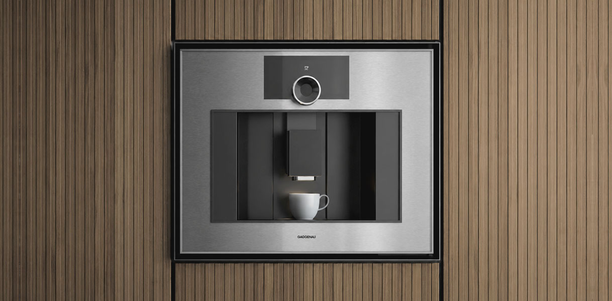 Gaggenau koffiemachine uit de Expressive serie met roestvrijstalen front achter rookglas in een houten keukenwand