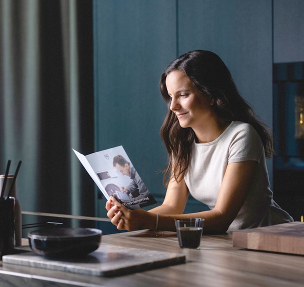 Vrouw leest V-ZUG brochure over uitgebreide garantievoorwaarden en 5 jaar standaard garantie op Zwitserse keukenapparatuur.