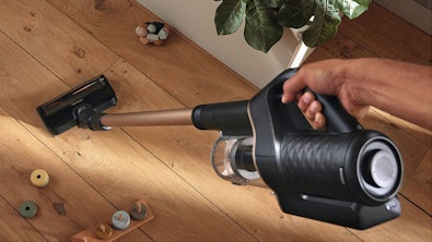 Handheld stofzuiger in gebruik op houten vloer met speelgoed toont wendbaarheid en gebruiksgemak