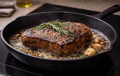 Geëmailleerde stalen koekenpan op inductie met biefstuk, knoflook en rozemarijn