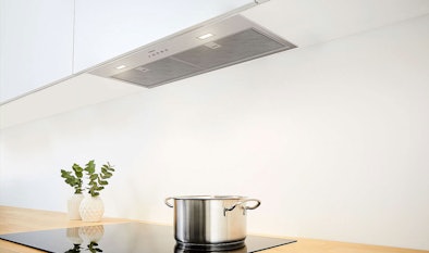 Geïntegreerde afzuigkap weggewerkt in een bovenkast met verlichting boven een kookplaat met pan