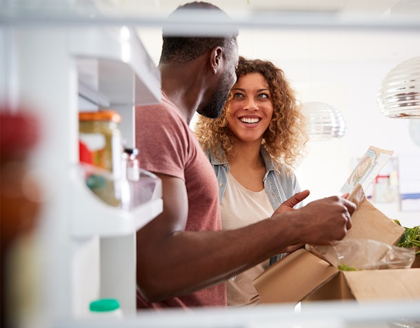 Man en vrouw kijken samen in een open koelkast terwijl ze boodschappen uitpakken.