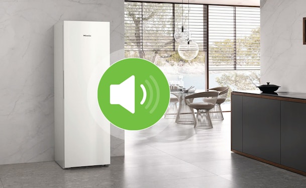 Staande vriezer in een open keuken met een geluidsniveau-icoon op de voorgrond.