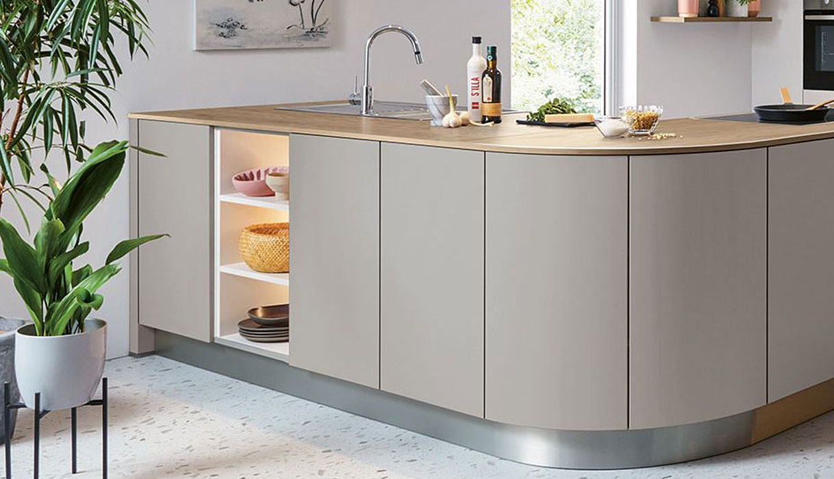 Greige keuken met afgerond kookeiland, licht houten werkblad, open nis met verlichting en moderne kraan in rustige, warme interieurstijl.