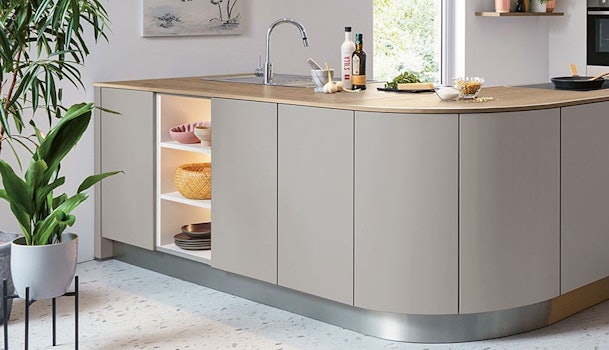 Greige keuken met afgerond kookeiland, licht houten werkblad, open nis met verlichting en moderne kraan in rustige, warme interieurstijl.