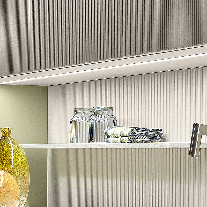 Ribbelachterwand met smalle legplank en onderbouwverlichting.