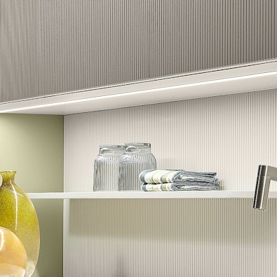 Ribbelachterwand met smalle legplank en onderbouwverlichting.