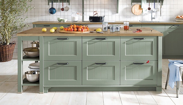 Saliegroene keuken met klassiek kookeiland, houten werkblad en witte tegelwand.