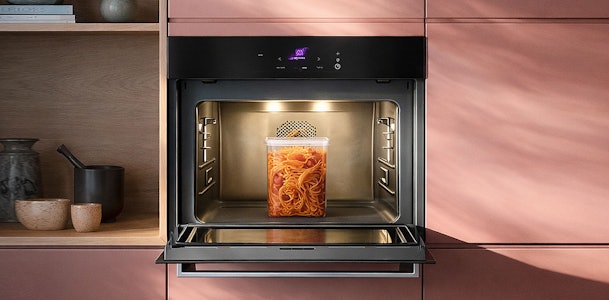 Grote solo magnetron ingebouwd in roze keukenkasten met pasta in glazen bak verlicht van binnenuit