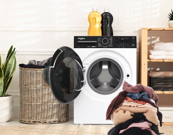 Grote Whirlpool-wasmachine met ruime trommel, open deur en een grote stapel wasgoed in een moderne wasruimte.