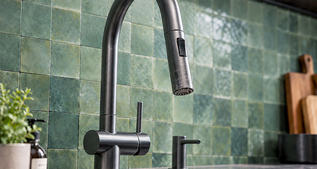 Gunmetal keukenkraan met zichtbare waterdruppels op de uitloop voor groene wandtegels