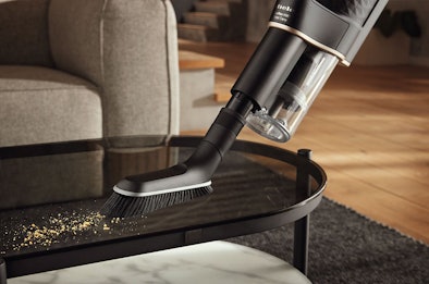 Handstofzuiger met accu zuigt kruimels op van zwarte salontafel in woonkamer