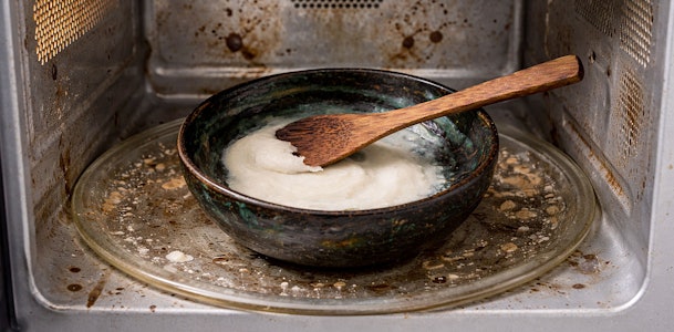 Kom met baking soda pasta en houten kwast in een vieze magnetron voor het verwijderen van hardnekkig vuil