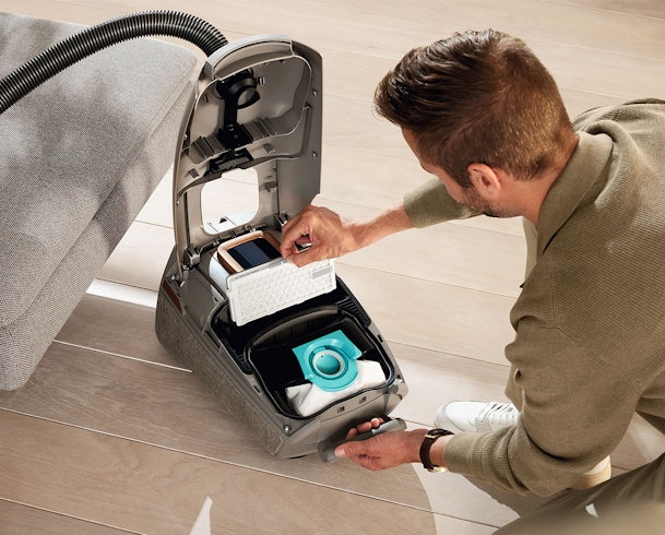 Man vervangt HEPA-filter stofzuiger onderhoud filterwisseling stofreservoir turquoise houder